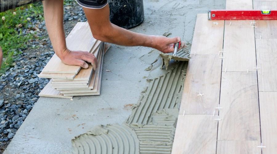 Mann nutzt Fliesenkleber im Garten - Terrassenplatten verlegen